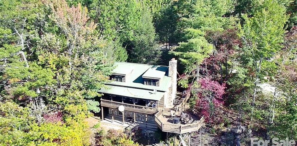 The cabin from above, green metal roof and stone chimney surrounded by fall woods