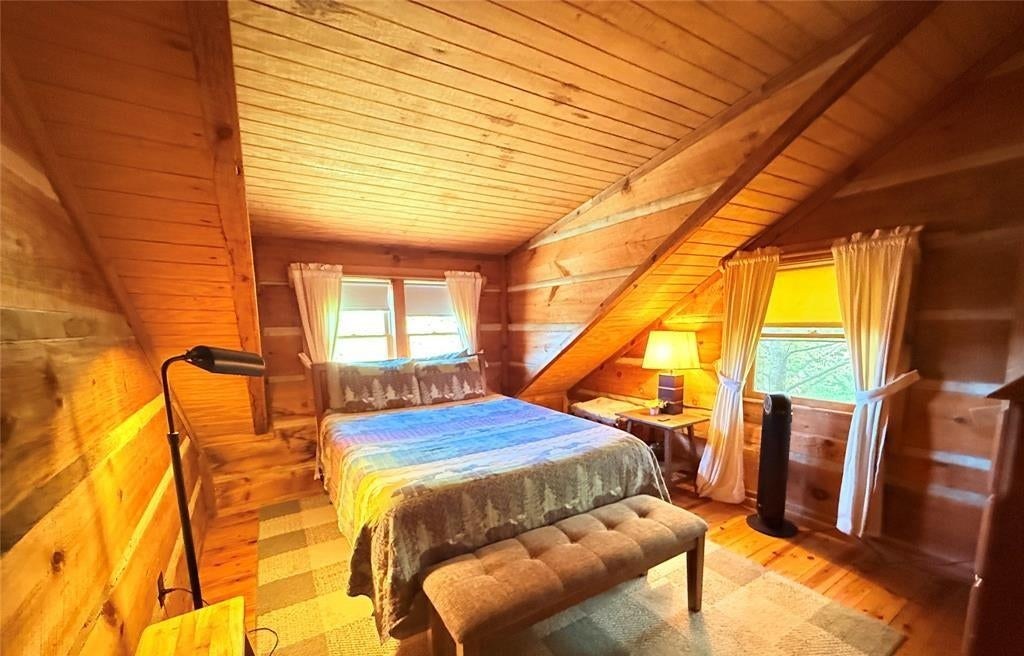 The second bedroom with a bed, bench and lamp under a sloped pine ceiling