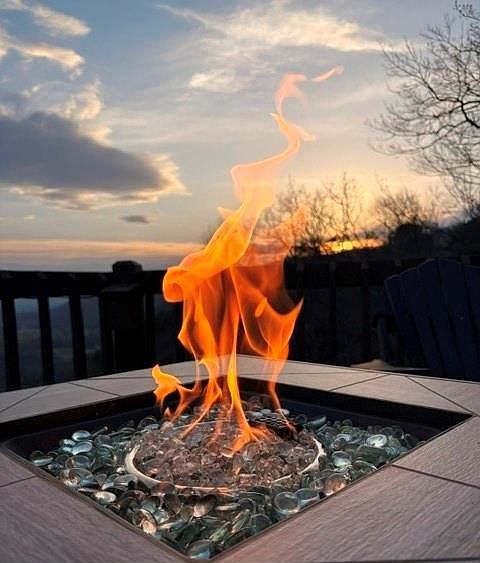 Flames rising from the deck fire table with the sun setting behind the ridge